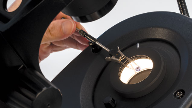 A gemologist analyzes a colored stone through a microscope