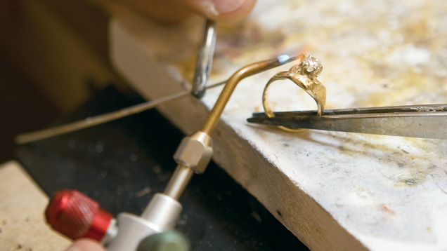 Hands holding jewelry repair tools and a ring